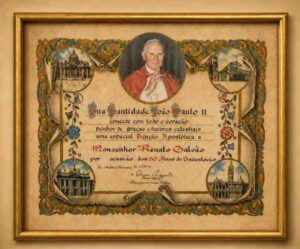 Uma bênção apostólica de São João Paulo II a Monsenhor Renato Galvão permanece preservada no Museu Casa do Sertão, da Universidade Estadual de Feira de Santana (Uefs), como uma das peças mais simbólicas da memória religiosa, cultural e educacional do município. O quadro integra o acervo da Biblioteca Setorial Monsenhor Renato Galvão e traz a mensagem concedida pelo então papa pelos 50 anos de sacerdócio do monsenhor. “Sua Santidade João Paulo II concede com todo o coração penhor de graças e favores celestiais uma especial Bênção Apostólica a Monsenhor Renato Galvão por ocasião dos 50 anos de Sacerdócio.”