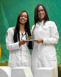 Cerimônia da Lamparina celebra compromisso de estudantes de Enfermagem da Uefs com o cuidado Em quarta edição, celebração reuniu estudantes do segundo semestre, familiares, docentes e representantes da universidade e do Coren-BA A luz de uma lamparina representa o conhecimento e a responsabilidade de cuidar da vida. Com esse simbolismo, o curso de Enfermagem da Universidade Estadual de Feira de Santana (Uefs) realizou, na sexta-feira (18), a quarta Cerimônia da Lamparina. A celebração reuniu estudantes do segundo semestre, familiares e docentes, reforçando o compromisso com uma formação pautada pela ética e pela humanidade. Participaram a reitora Amali Mussi, a pró-reitora de Ensino de Graduação, Rosa Eugênia Santana, e a enfermeira Fabia Quele, representante do Conselho Regional de Enfermagem da Bahia (Coren-BA). O encontro marcou uma etapa da trajetória acadêmica dos futuros profissionais, com a participação de pessoas que acompanham e apoiam esse percurso. Memória da profissão A tradição remete à atuação de Florence Nightingale, considerada precursora da enfermagem moderna, durante a Guerra da Crimeia, no século XIX. Com uma lamparina, ela percorria as enfermarias à noite para acompanhar os soldados feridos. As rondas lhe renderam o reconhecimento como Dama da Lâmpada, e o objeto se tornou um dos símbolos da enfermagem. Também chamada de Cerimônia da Lâmpada, a celebração integra atividades de formação em outras instituições de ensino. Na Uefs, a chama representa a dedicação e o conhecimento que devem acompanhar os estudantes ao longo da formação e do exercício profissional. “A chama simboliza a luz do conhecimento, a dedicação e o compromisso que passam a acompanhar cada futuro profissional no cuidado ao paciente”, destaca a professora Aisiane Cedraz Morais, coordenadora do Colegiado de Enfermagem. Cuidado e humanidade O significado da cerimônia ultrapassa a preparação técnica. Segundo as informações encaminhadas pelo curso, a celebração reforça a responsabilidade de cuidar com respeito, empatia, ética e humanidade. A lamparina acesa simboliza a orientação necessária diante de cada encontro, de cada desafio e de cada vida confiada aos cuidados da enfermagem. A presença de familiares e docentes aproxima a comunidade acadêmica desse compromisso e valoriza a rede de apoio aos estudantes. Ao conectar a memória da profissão à formação universitária, a cerimônia reafirma o cuidado humano como parte essencial da construção do conhecimento em enfermagem.