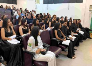 Cerimônia da Lamparina celebra compromisso de estudantes de Enfermagem da Uefs com o cuidado Em quarta edição, celebração reuniu estudantes do segundo semestre, familiares, docentes e representantes da universidade e do Coren-BA A luz de uma lamparina representa o conhecimento e a responsabilidade de cuidar da vida. Com esse simbolismo, o curso de Enfermagem da Universidade Estadual de Feira de Santana (Uefs) realizou, na sexta-feira (18), a quarta Cerimônia da Lamparina. A celebração reuniu estudantes do segundo semestre, familiares e docentes, reforçando o compromisso com uma formação pautada pela ética e pela humanidade. Participaram a reitora Amali Mussi, a pró-reitora de Ensino de Graduação, Rosa Eugênia Santana, e a enfermeira Fabia Quele, representante do Conselho Regional de Enfermagem da Bahia (Coren-BA). O encontro marcou uma etapa da trajetória acadêmica dos futuros profissionais, com a participação de pessoas que acompanham e apoiam esse percurso. Memória da profissão A tradição remete à atuação de Florence Nightingale, considerada precursora da enfermagem moderna, durante a Guerra da Crimeia, no século XIX. Com uma lamparina, ela percorria as enfermarias à noite para acompanhar os soldados feridos. As rondas lhe renderam o reconhecimento como Dama da Lâmpada, e o objeto se tornou um dos símbolos da enfermagem. Também chamada de Cerimônia da Lâmpada, a celebração integra atividades de formação em outras instituições de ensino. Na Uefs, a chama representa a dedicação e o conhecimento que devem acompanhar os estudantes ao longo da formação e do exercício profissional. “A chama simboliza a luz do conhecimento, a dedicação e o compromisso que passam a acompanhar cada futuro profissional no cuidado ao paciente”, destaca a professora Aisiane Cedraz Morais, coordenadora do Colegiado de Enfermagem. Cuidado e humanidade O significado da cerimônia ultrapassa a preparação técnica. Segundo as informações encaminhadas pelo curso, a celebração reforça a responsabilidade de cuidar com respeito, empatia, ética e humanidade. A lamparina acesa simboliza a orientação necessária diante de cada encontro, de cada desafio e de cada vida confiada aos cuidados da enfermagem. A presença de familiares e docentes aproxima a comunidade acadêmica desse compromisso e valoriza a rede de apoio aos estudantes. Ao conectar a memória da profissão à formação universitária, a cerimônia reafirma o cuidado humano como parte essencial da construção do conhecimento em enfermagem.