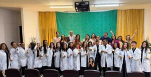 Cerimônia da Lamparina celebra compromisso de estudantes de Enfermagem da Uefs com o cuidado Em quarta edição, celebração reuniu estudantes do segundo semestre, familiares, docentes e representantes da universidade e do Coren-BA A luz de uma lamparina representa o conhecimento e a responsabilidade de cuidar da vida. Com esse simbolismo, o curso de Enfermagem da Universidade Estadual de Feira de Santana (Uefs) realizou, na sexta-feira (18), a quarta Cerimônia da Lamparina. A celebração reuniu estudantes do segundo semestre, familiares e docentes, reforçando o compromisso com uma formação pautada pela ética e pela humanidade. Participaram a reitora Amali Mussi, a pró-reitora de Ensino de Graduação, Rosa Eugênia Santana, e a enfermeira Fabia Quele, representante do Conselho Regional de Enfermagem da Bahia (Coren-BA). O encontro marcou uma etapa da trajetória acadêmica dos futuros profissionais, com a participação de pessoas que acompanham e apoiam esse percurso. Memória da profissão A tradição remete à atuação de Florence Nightingale, considerada precursora da enfermagem moderna, durante a Guerra da Crimeia, no século XIX. Com uma lamparina, ela percorria as enfermarias à noite para acompanhar os soldados feridos. As rondas lhe renderam o reconhecimento como Dama da Lâmpada, e o objeto se tornou um dos símbolos da enfermagem. Também chamada de Cerimônia da Lâmpada, a celebração integra atividades de formação em outras instituições de ensino. Na Uefs, a chama representa a dedicação e o conhecimento que devem acompanhar os estudantes ao longo da formação e do exercício profissional. “A chama simboliza a luz do conhecimento, a dedicação e o compromisso que passam a acompanhar cada futuro profissional no cuidado ao paciente”, destaca a professora Aisiane Cedraz Morais, coordenadora do Colegiado de Enfermagem. Cuidado e humanidade O significado da cerimônia ultrapassa a preparação técnica. Segundo as informações encaminhadas pelo curso, a celebração reforça a responsabilidade de cuidar com respeito, empatia, ética e humanidade. A lamparina acesa simboliza a orientação necessária diante de cada encontro, de cada desafio e de cada vida confiada aos cuidados da enfermagem. A presença de familiares e docentes aproxima a comunidade acadêmica desse compromisso e valoriza a rede de apoio aos estudantes. Ao conectar a memória da profissão à formação universitária, a cerimônia reafirma o cuidado humano como parte essencial da construção do conhecimento em enfermagem.
