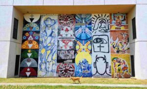 Ateliê Udo Knoff e 12 artistas transformam a Reitoria da Uefs em galeria a céu aberto Dois grandes murais de azulejos integram arte e arquitetura no campus e valorizam diferentes expressões da cultura nordestina Nas paredes laterais da Reitoria da Universidade Estadual de Feira de Santana (Uefs), a arte participa do cotidiano de quem estuda, trabalha ou visita o campus. Datado de 2002, o conjunto formado por dois grandes murais de azulejos transforma o prédio em uma galeria a céu aberto, com figuras, símbolos e composições que convidam à observação e aproximam a comunidade universitária da produção artística baiana. São 12 painéis, seis de cada lado, com obras de Antônio Brasileiro, Bel Borba, Juraci Dórea, Justino Marinho, Washington Falcão, Juarez Paraíso, Chico Liberato, Reinaldo Eckenberger, Sônia Rangel, César Romero, J. Cunha e Márcia Magno. A variedade de linguagens permite reconhecer diferentes trajetórias e maneiras de interpretar a cultura, compondo um conjunto de forte presença na paisagem universitária. Uma escolha que valoriza a diversidade A iniciativa merece reconhecimento tanto pela dimensão monumental dos murais quanto pela decisão de prestigiar diversos artistas consagrados. Cada autor recebeu uma ampla superfície para desenvolver uma criação própria. A reunião dessas obras valoriza a pluralidade da arte baiana e demonstra como diferentes estilos podem compartilhar um espaço sem perder a identidade. Os murais estão ligados ao Projeto Nordeste de Artes Plásticas, movimento que promoveu exposições, encontros e intercâmbios na região durante a década de 1980. Na Uefs, esse espírito coletivo ganhou permanência na arquitetura. O conjunto amplia a experiência de estar no campus e reafirma a importância da arte na formação cultural, no exercício da sensibilidade e na construção da memória. O legado do Ateliê Udo Knoff Os azulejos foram confeccionados no Ateliê Cerâmico Udo Knoff, em Salvador. Fundado pelo ceramista alemão radicado na Bahia e instalado no bairro de Brotas, o espaço tornou-se referência na integração entre arte e arquitetura. Knoff executou composições de diferentes artistas e incentivou a exploração da cerâmica como linguagem. A transferência dos desenhos, a pintura e a queima das peças reuniam criação artística, trabalho artesanal e conhecimento técnico. A permanência desse patrimônio exige cuidado contínuo. Em visita ao local, foi possível observar perda de brilho em parte dos azulejos do lado oeste do prédio, que recebe o sol da tarde. A observação reforça a importância de uma avaliação especializada para identificar as causas e orientar a conservação. Preservar os murais é também proteger a memória dos artistas e uma iniciativa que deu à arte lugar de destaque na universidade. Everaldo Goes | © Feira Hoje Siga @feirahoje 11/10/26