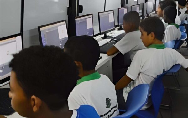 Computação na rede municipal de Feira vai além de aprender a usar o computador Diretrizes preveem raciocínio lógico, compreensão das tecnologias e uso responsável da internet, com implantação gradual e conteúdos integrados ao currículo Resolver problemas, compreender como as tecnologias funcionam e aprender a avaliar as informações que circulam na internet. Esses são alguns dos objetivos do ensino de Computação na Educação Básica, que ganhou um novo encaminhamento na rede municipal de Feira de Santana. Em notícia publicada em 13 de outubro, a Prefeitura informou a adesão às diretrizes curriculares da Bahia, formalizada pelo Conselho Municipal de Educação por meio da Resolução nº 030/2026. A implantação será gradual, acompanhada de formação dos profissionais e incorporada ao planejamento das escolas. A proposta organiza a aprendizagem em três eixos. O pensamento computacional desenvolve a capacidade de dividir problemas em partes, identificar padrões e estabelecer passos para encontrar soluções. O mundo digital envolve a compreensão de equipamentos, redes e do armazenamento e da circulação de dados. Já a cultura digital trata da participação consciente, crítica e responsável nos ambientes tecnológicos. Na prática, a formação busca dar aos estudantes condições de compreender e utilizar a tecnologia com maior autonomia. Aprendizagem também sem telas Na educação infantil, essa abordagem pode envolver brincadeiras de organizar objetos, reconhecer repetições e seguir sequências de instruções. São possibilidades da chamada computação desplugada, realizada sem computador. A Resolução CME nº 90/2025, publicada em agosto do ano passado, já previa atividades lúdicas e exploração de padrões nessa etapa. Para o ensino fundamental, estabelecia a introdução progressiva de programação, robótica e projetos interdisciplinares. Na Educação de Jovens e Adultos, a orientação é trabalhar situações do cotidiano e tecnologias acessíveis. O mesmo documento municipal define a Computação como componente transversal e integrador, articulado às demais áreas do currículo. Assim, uma atividade de Matemática pode explorar sequências e soluções para problemas, enquanto uma proposta de leitura pode estimular a avaliação das informações recebidas. Esses são exemplos possíveis de aplicação. A norma também atribui à Secretaria Municipal de Educação a responsabilidade de assegurar infraestrutura tecnológica mínima, materiais pedagógicos e formação continuada dos professores. Feira integra orientação nacional A mudança faz parte de um movimento mais amplo. Em 2022, o Conselho Nacional de Educação estabeleceu as normas de Computação como complemento à Base Nacional Comum Curricular. As diretrizes nacionais de educação digital e midiática de 2025 fixaram o início da implementação dos novos currículos em 2026. Na Bahia, a regulamentação estadual admite a adesão dos sistemas municipais, respeitando a autonomia de cada rede. A decisão de Feira insere-se nesse processo, com a expectativa de desenvolver raciocínio lógico, criatividade, segurança digital e capacidade de analisar informações. A rede em Feira de Santana já registra ações relacionadas ao tema. Em março deste ano, uma formação dos profissionais dos anos iniciais apresentou o projeto MicroKids, associado pela Seduc às diretrizes da BNCC Computação. Em abril, professores receberam orientações sobre a plataforma e o uso de recursos tecnológicos em diferentes componentes curriculares. A resolução de 2026 determina que as escolas incorporem as competências e habilidades aos projetos pedagógicos e prevê acompanhamento pela Secretaria de Educação e pelo Conselho Municipal. O documento não estabelece datas de implantação por escola, valores de investimento ou quantitativos de equipamentos. Computação na Educação Básica, educação digital, Feira de Santana, rede municipal de ensino, BNCC Computação, pensamento computacional, cultura digital, formação de professores, Conselho Municipal de Educação, Secretaria Municipal de Educação Por Everaldo Goes, com informações Ministério da Educação, Secretaria de Educação do Estado e Secretaria Municipal de Educação  Siga @feirahoje 15/10/26