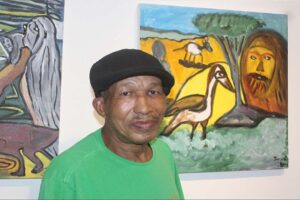 Por onde anda Tonho da Bahia? Em setembro de 2022, Tonho da Bahia ocupava o centro das atenções na reabertura da Galeria de Arte Carlo Barbosa, do Centro Universitário de Cultura e Arte (Cuca), da Uefs. Os quadros de José Antônio dos Santos Pereira levavam para aquele espaço as cores e o cotidiano de Feira de Santana. Quatro anos depois, cabe perguntar à Universidade o que ocorreu com a trajetória artística que a própria instituição ajudou a revelar. Auxiliar de serviços gerais e trabalhador terceirizado, Tonho encontrou no ambiente onde trabalhava uma oportunidade de formação. Em 2014, aos 54 anos, começou a participar das oficinas do Cuca. Aprendeu desenho com Avelina Bitencourt e pintura com Jorge Galeano. Em 2017, uma obra foi selecionada para a Bienal Internacional de Arte Naïf Totem Cor-Ação, em Socorro, no interior de São Paulo. Na exposição de 2022, o então reitor Evandro do Nascimento afirmou que a iniciativa “cumpre um papel de valorizar a obra de um artista da terra”. Também destacou que Tonho “tem um estilo muito próprio de uso de determinadas cores, mas com a temática muito presente na nossa realidade de Feira de Santana e de nossa região”. Defendeu, ainda, esforços de valorização “dos nossos potenciais”. Há pelo menos um registro institucional posterior. A programação da Feira de Graduação da Uefs, em outubro de 2024, anunciou a exposição de uma obra de Tonho entre as atividades do Cuca. Esse anúncio, entretanto, não esclarece como prosseguiu a produção do artista, quais oportunidades recebeu desde então ou qual relação mantém atualmente com o centro de cultura. Ou se ele foi convidado e esteve presente.  Esquecimento  Tonho continua pintando? Participa de oficinas e exposições? Permanece trabalhando na Universidade? Houve transferência do Cuca para o campus e, em caso positivo, por qual motivo? Que acompanhamento e incentivo à produção artística foram mantidos? São perguntas dirigidas à Uefs e ao Cuca sobre uma trajetória apresentada publicamente como exemplo dos resultados da formação cultural. A história de Tonho merece continuidade e visibilidade. Ao reconhecer naquele trabalhador um artista capaz de representar Feira de Santana, a Universidade mostrou o alcance de uma oportunidade. Agora, não pode simplesmente deixar no esquecimento. Cabe esclarecer os caminhos dessa trajetória e quais possibilidades existem para que o público volte a encontrar Tonho da Bahia e a produção dele. 18/10/26